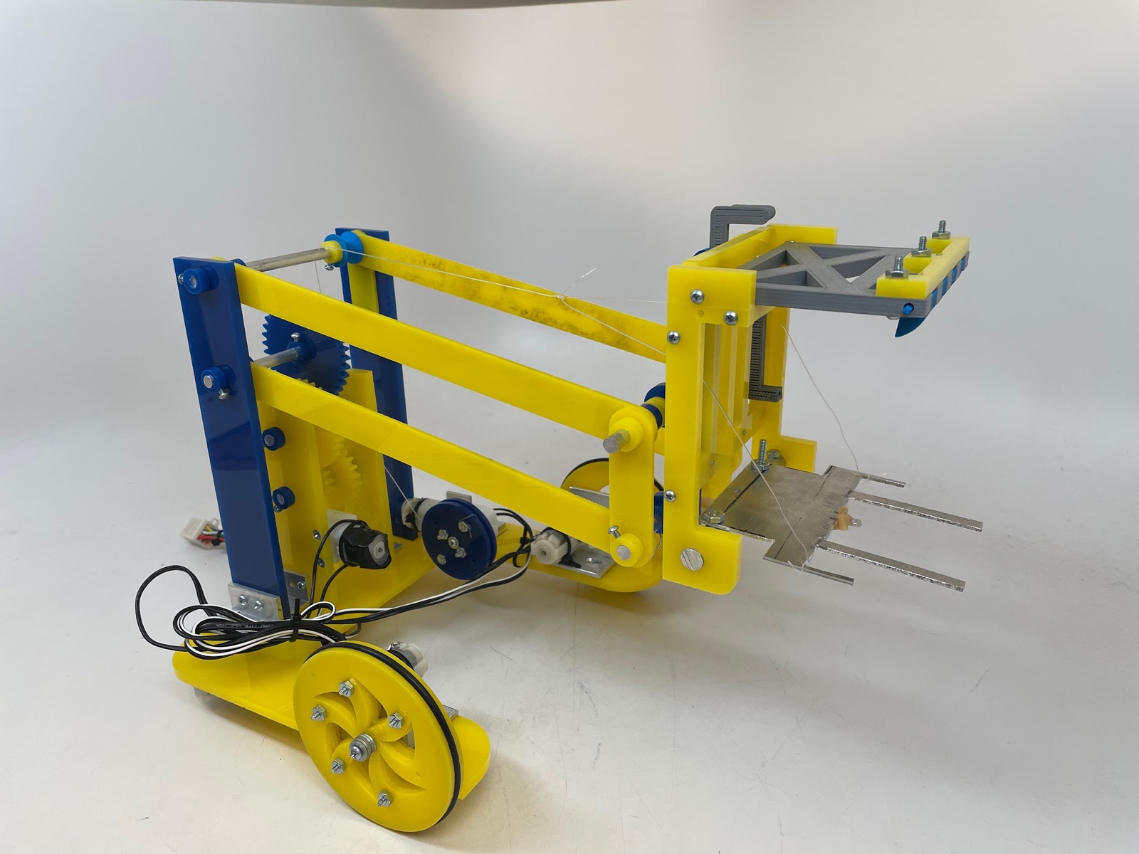 The finished robot: a yellow acrylic four-bar lift on blue uprights, a gearbox, two large wheels, and a fork-and-fangs claw at the end